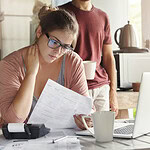 Woman reviewing financial documents with concern in a kitchen setting.