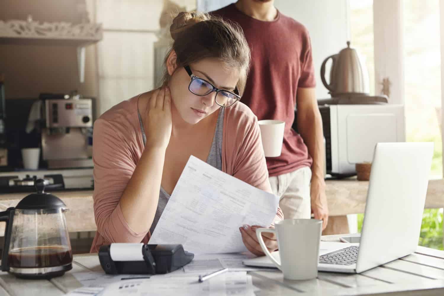 Woman reviewing financial documents with concern in a kitchen setting.
