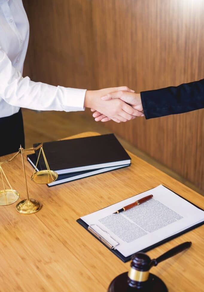 Handshake between two professionals over legal documents in an office setting.
