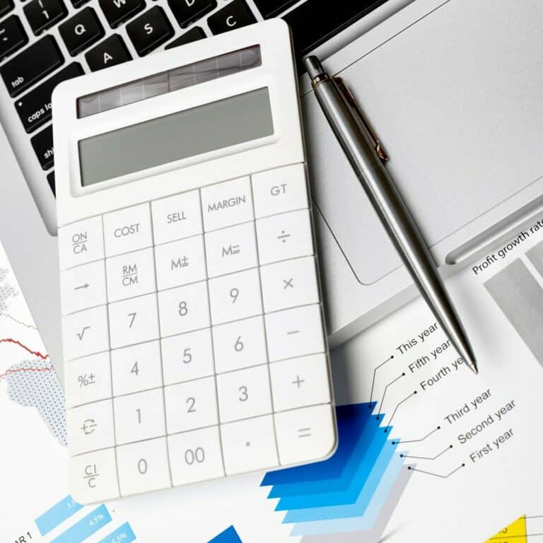 Calculator and pen on financial documents with a laptop in the background.