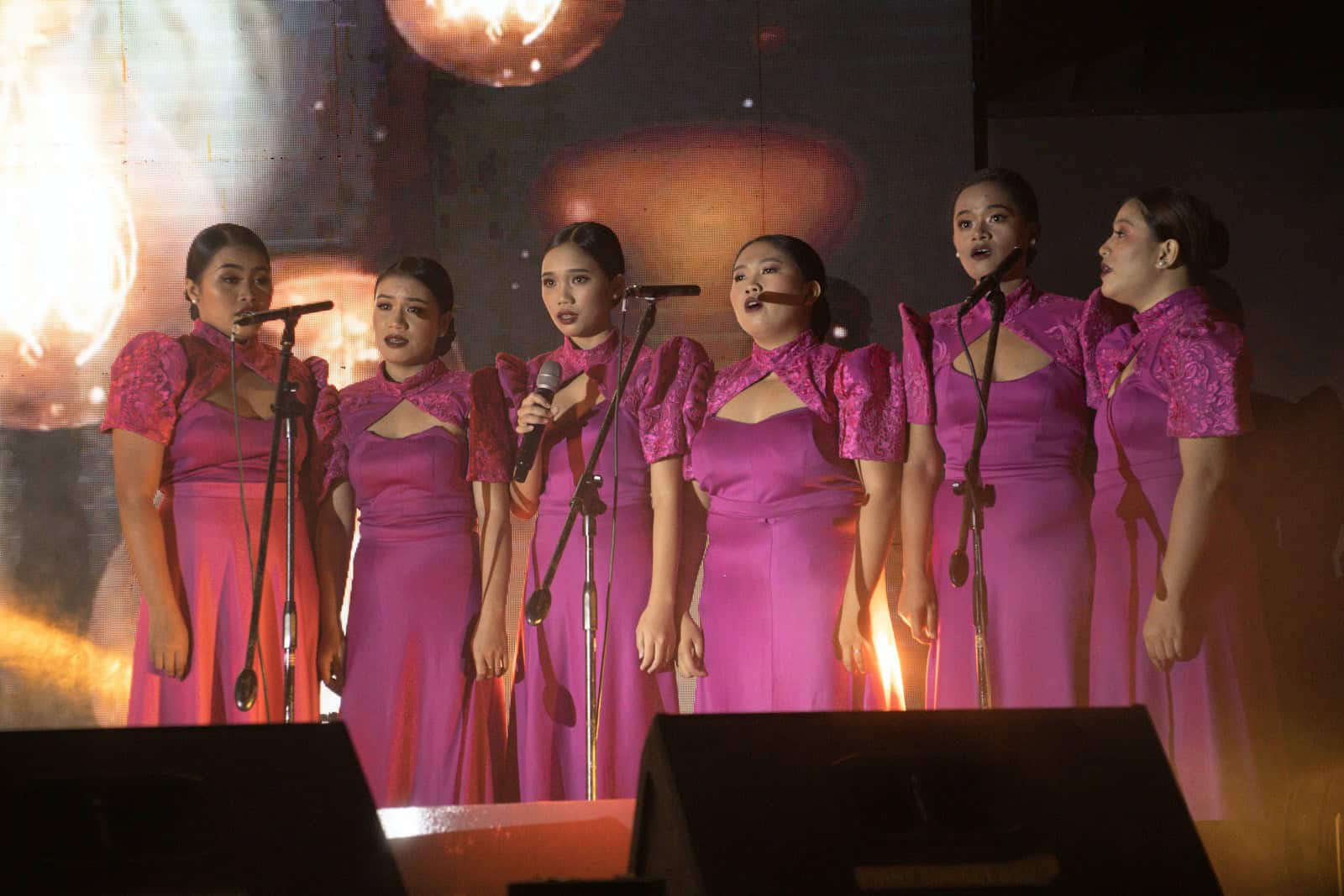 a group of women in pink dresses singing into microphones