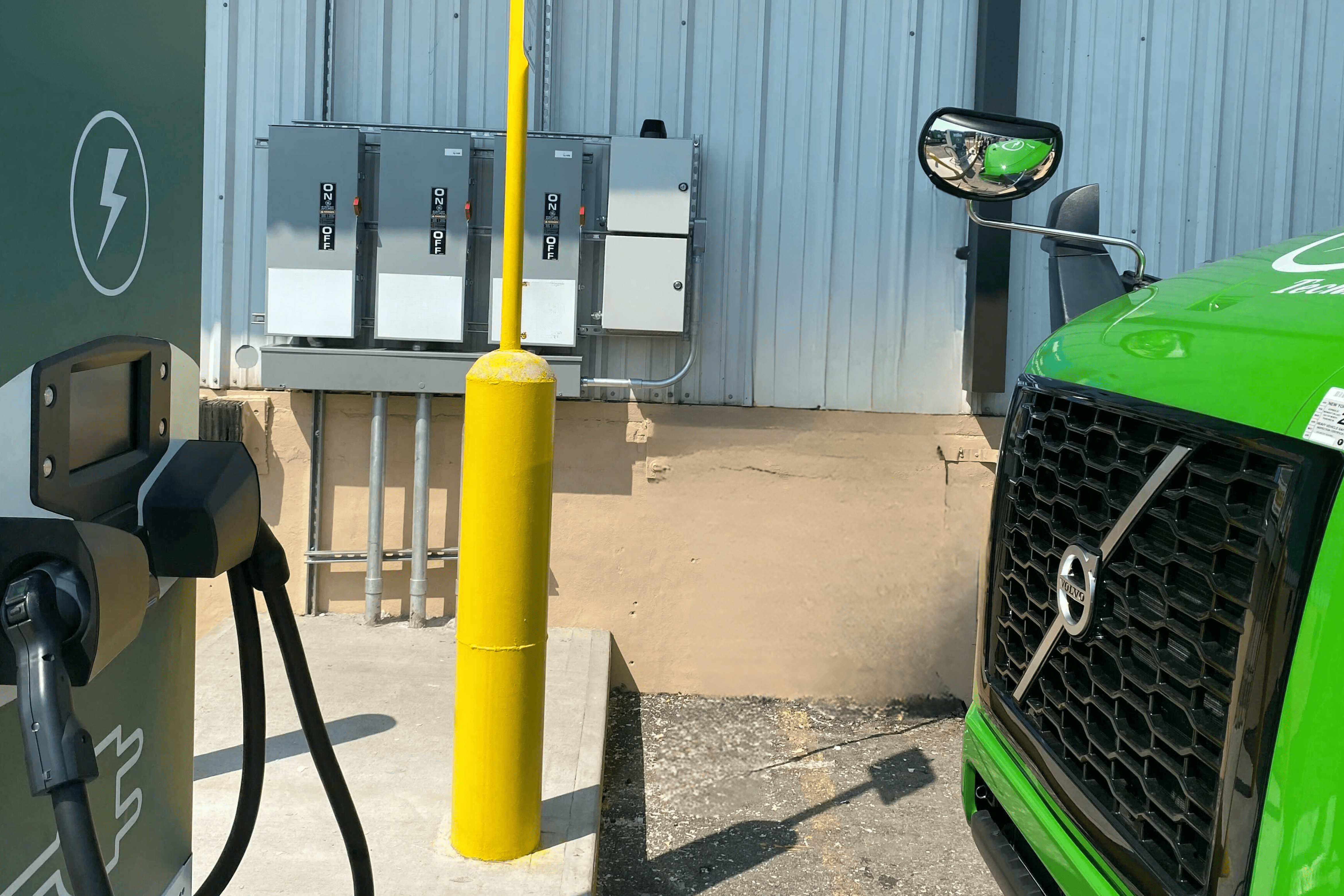 Electric vehicle charging station with a green EV and utility boxes behind it.