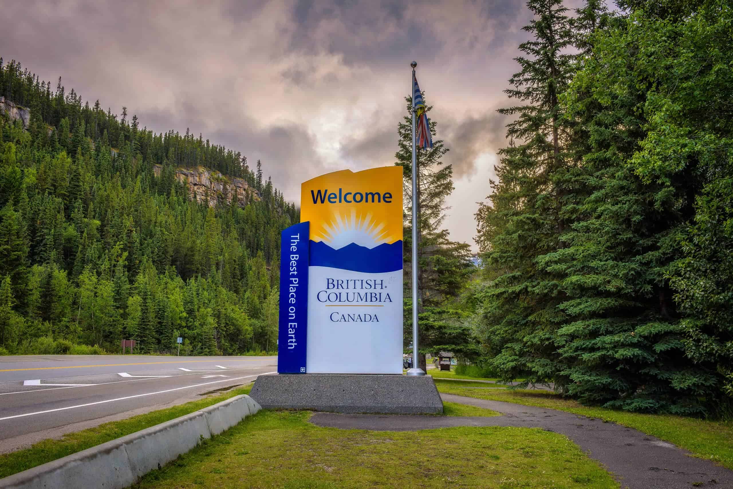 British Columbia welcoming sign in Canada, lush forest and cloudy sky background.