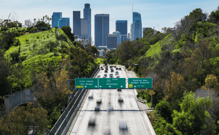 Clear cityscape of Los Angeles with highway leading to downtown, green hills, and skyscrapers.
