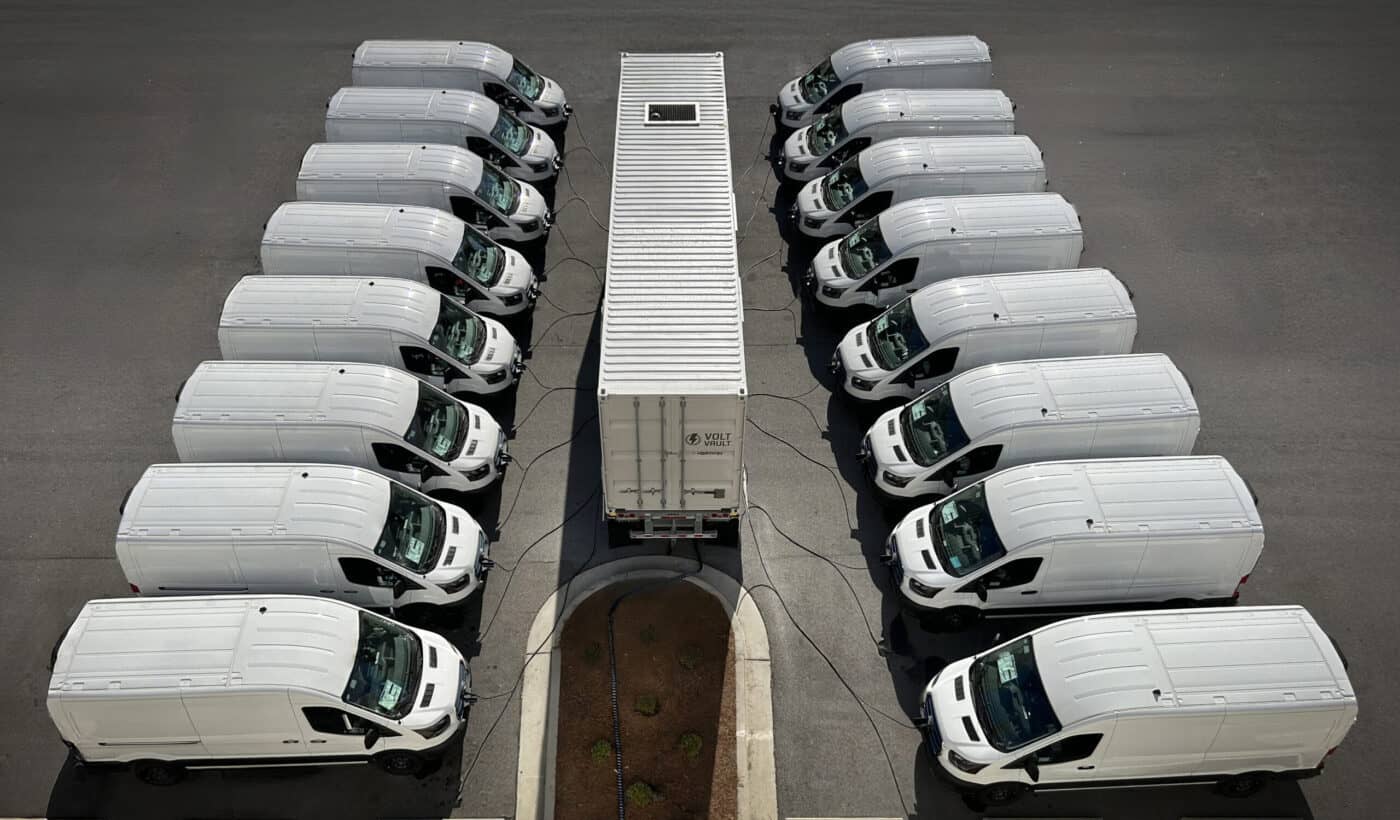 Electric delivery vans charging at a renewable energy-powered charging station for sustainable transportation.