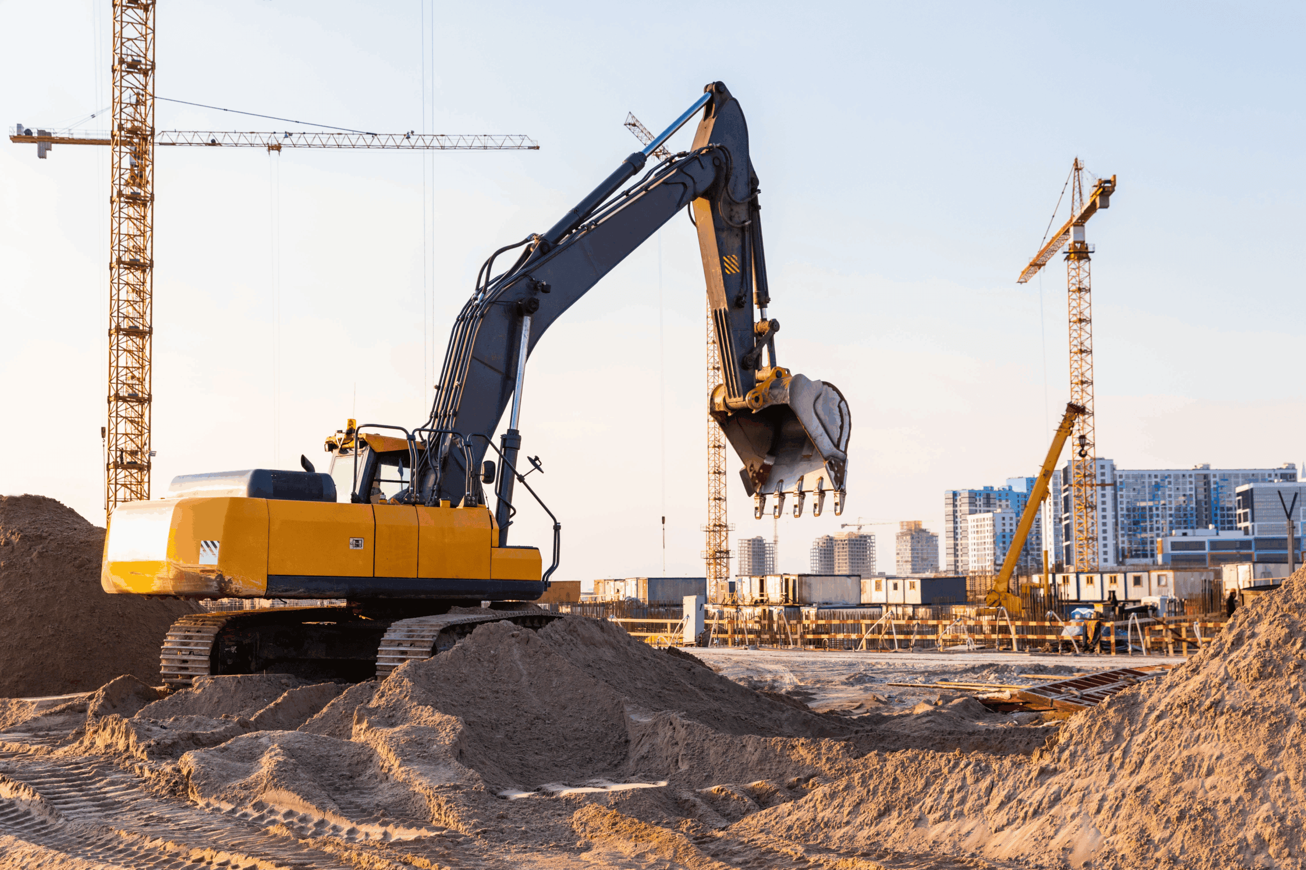 Construction excavator at U.S. energy infrastructure site with cranes and cityscape in background.