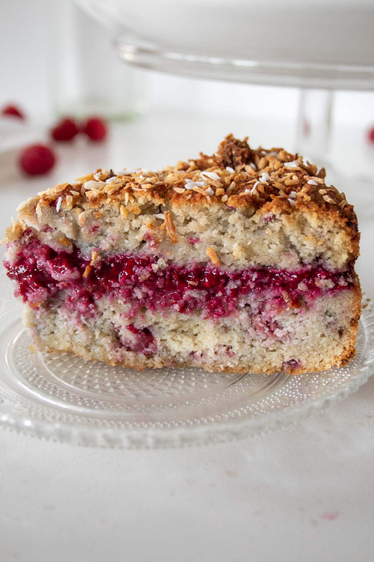 closeup of a slice of coconut raspberry cake on a plate with a layer of homemade sugar free jam