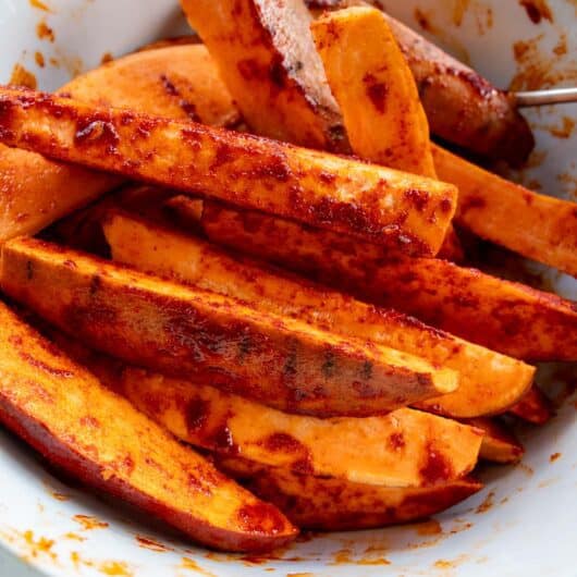 raw sweet potato wedges mixed with smoked paprika seasoning in a bowl