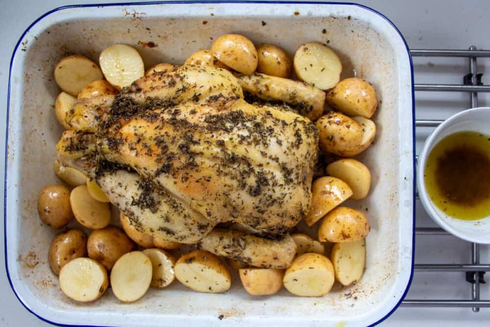 Part cooked roast chicken with raw baby potatoes and a bowl of meat juices