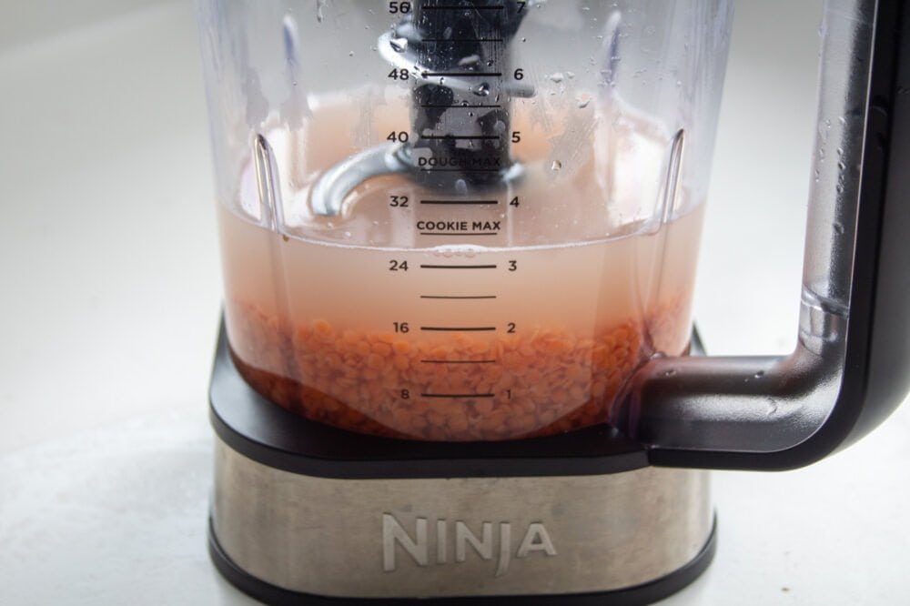 red lentils soaking in water in the jug of the food processor