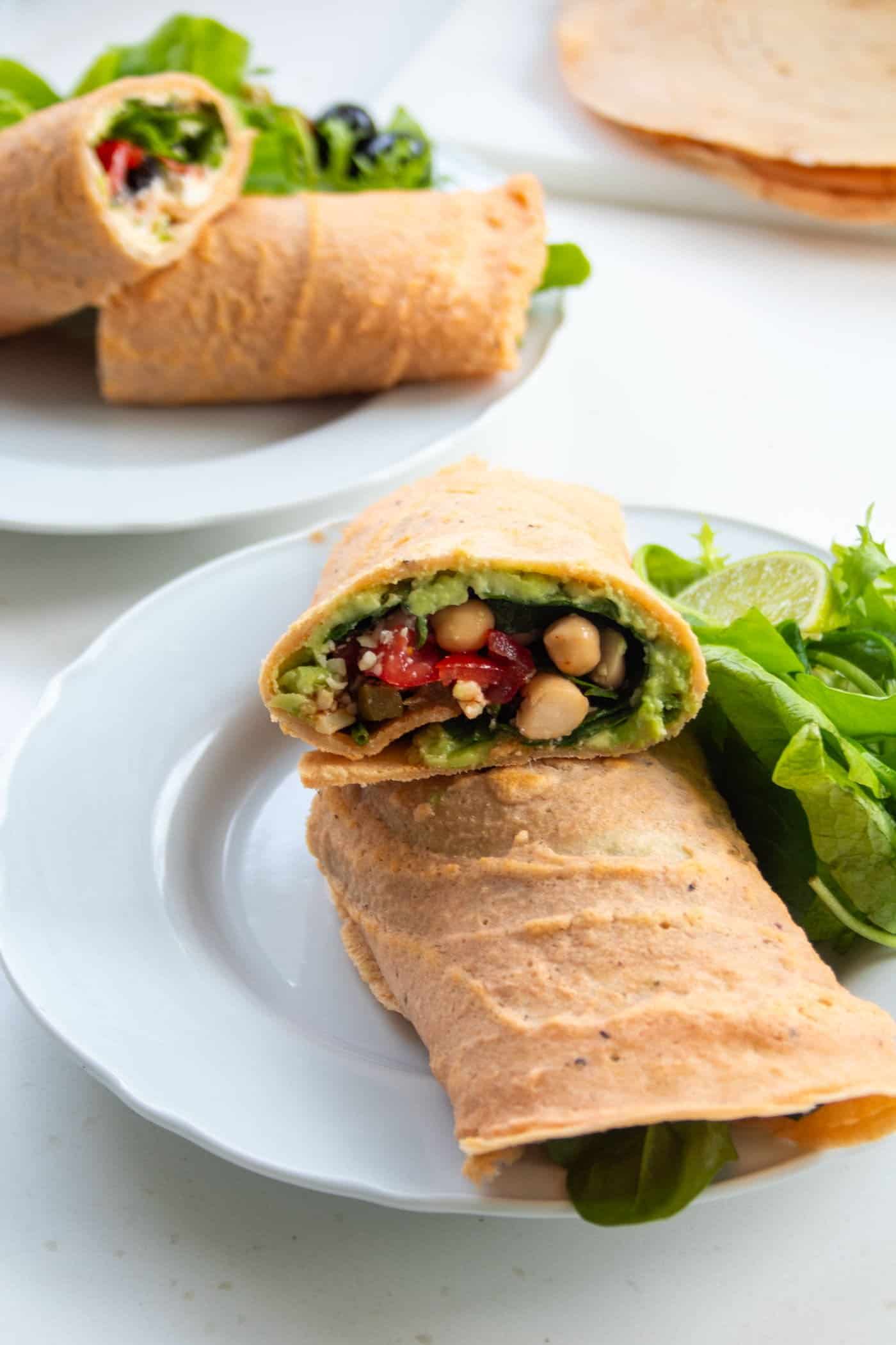 A filled and rolled lentil wrap on a plate with salad leaves