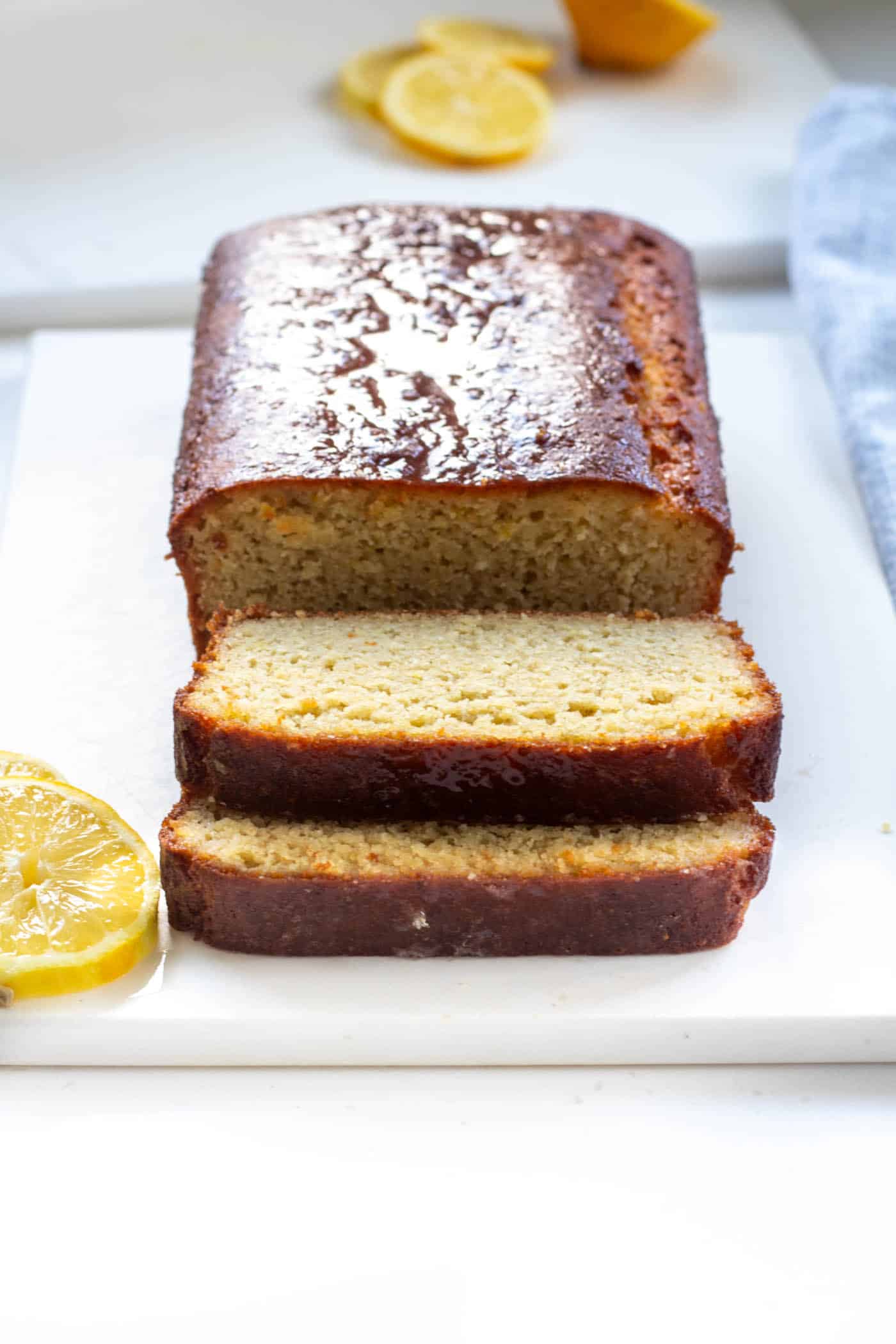 a sliced lemon drizzle loaf on a white board with lemon slices