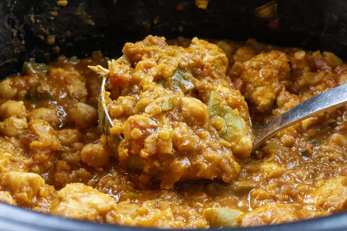 A black slow cooker bowl filled with chicken curry and a ladel with a scoop of slow cooked chicken curry