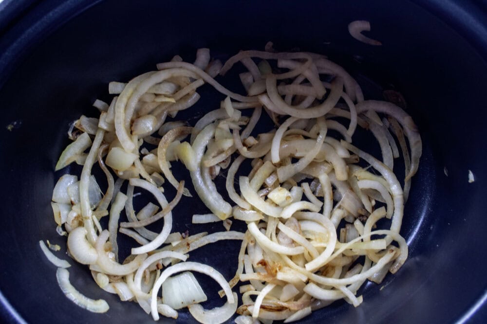 A black slow cooker bowl filled with the browned onions