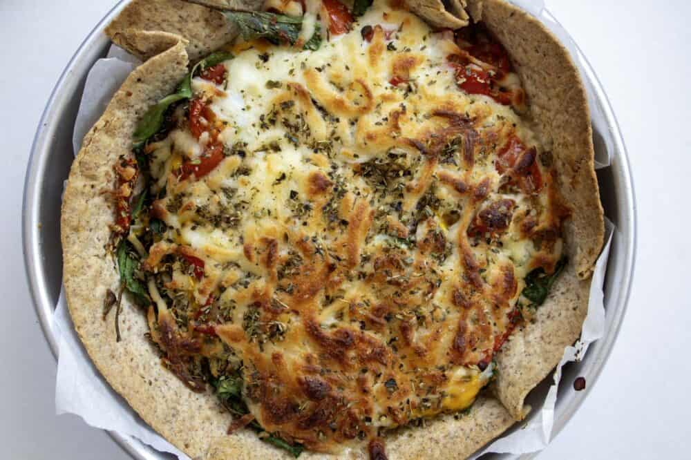 cooked healthy breakfast tortilla pizza in a round cake tin with greaseproof paper