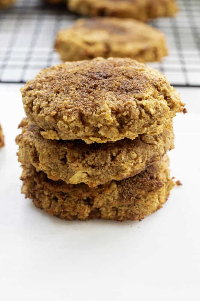 a stack of of three large Pumpkin oat cookies and on a white surface with a rack of cookies in the background