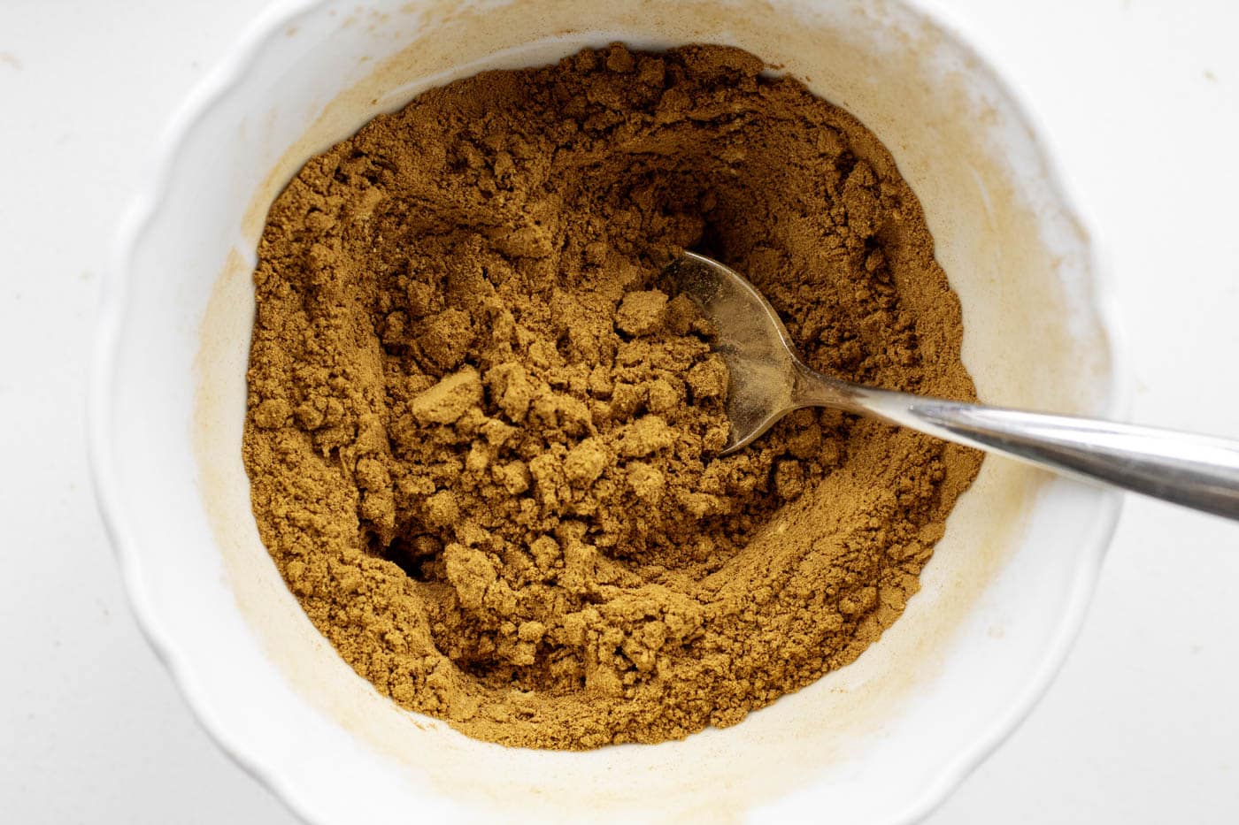pumpkin pie spices mixed in a white bowl with a teaspoon