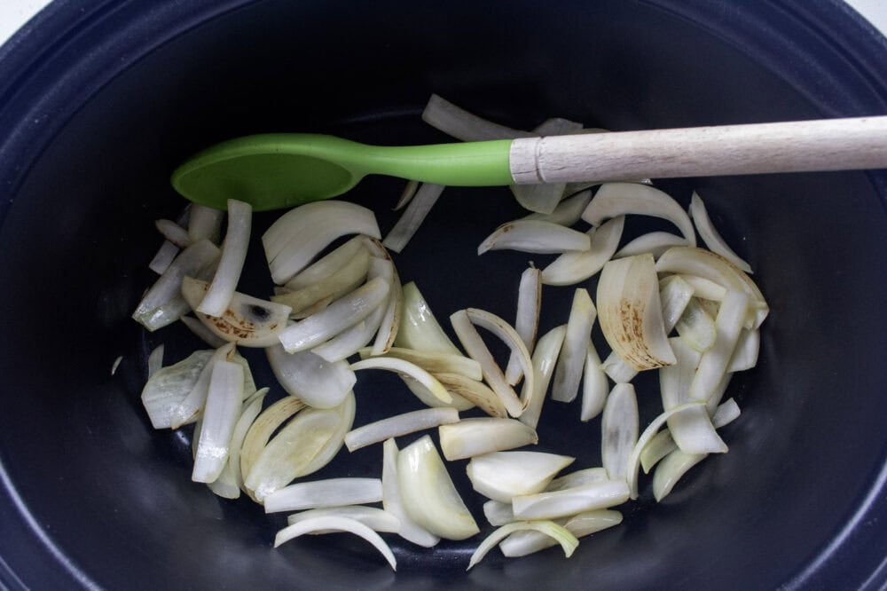 sliced onions in the crockpot bowl with a green silicone spoon