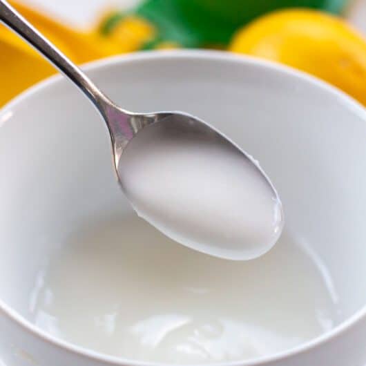 sugar free lemon icing on a silver spoon over a bowl with a lemon and lemon squeezer in the background