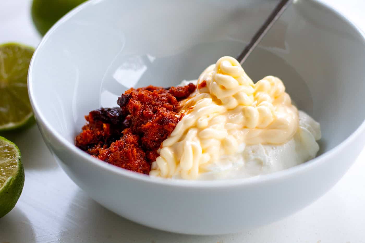 ingredients for chipotle sauce in a bowl with a spoon including greey yogurt, mayonnaise, sun dried tomato paste and chipotle paste