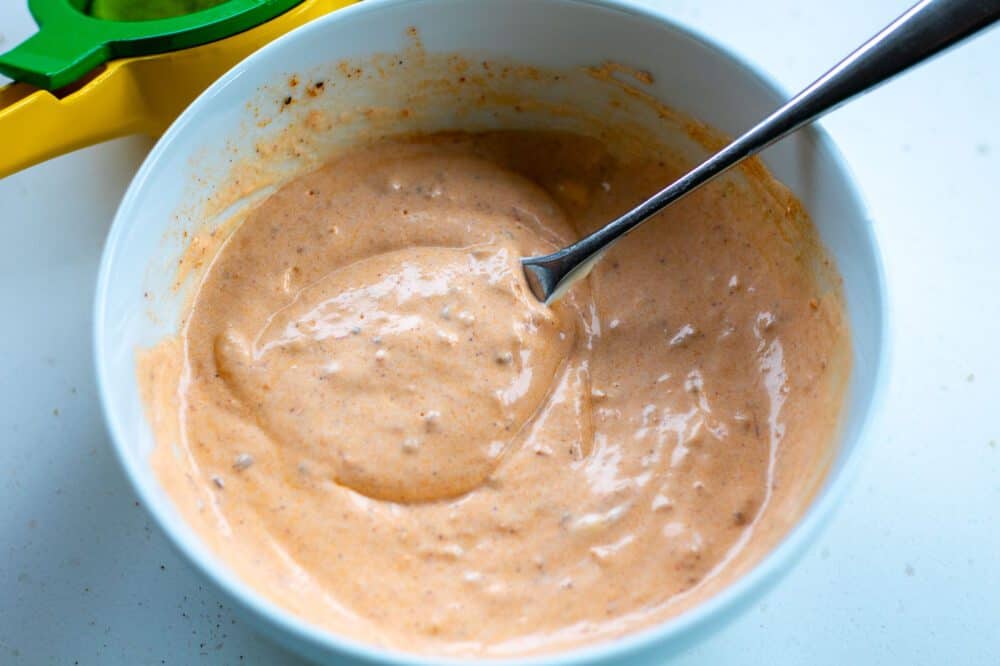 Mixed chipotle dressing in a bowl witha spoon and the lime squeezer in the background