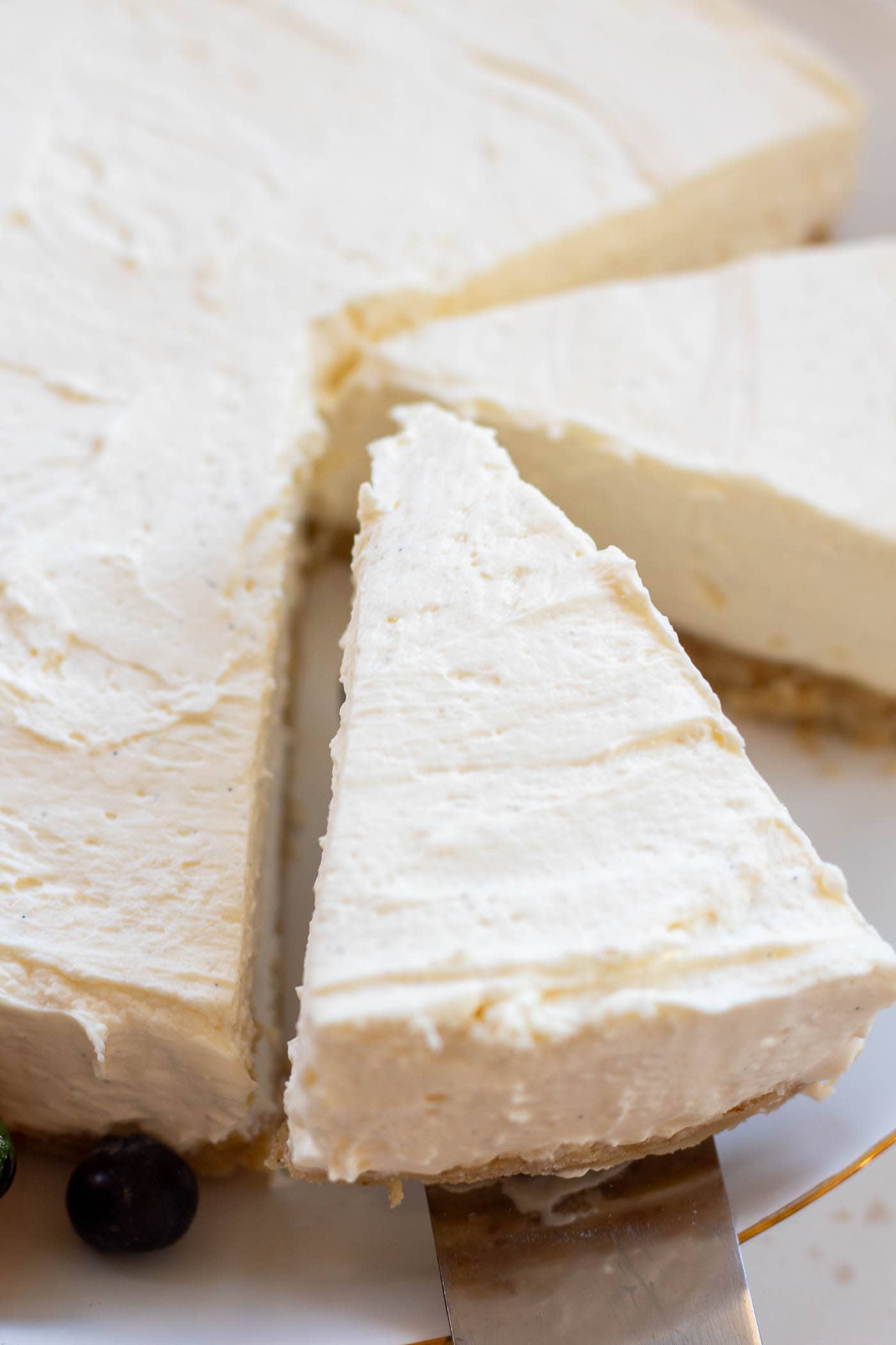 Looking down onto a slice of sugar-free vanilla cheesecake being gently lifted up from the plate with the whole cheesecake on.