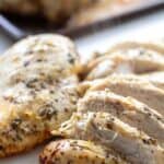 sliced and tender oven roasted lemon and garlic Greek marinated chicken breasts on a white chopping board with the baking tray in the background
