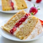 A closeup of a Slice of low carb sponge cake with strawberry jam and cream filling, ideal for diabetic-friendly afternoon tea with another slice and fresh strawberries in the background