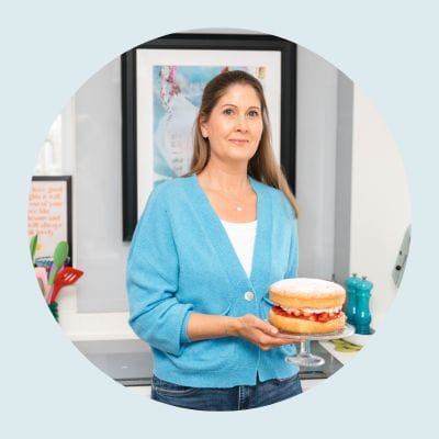 Michelle Rorke, founder of Whole Hearty Kitchen, smiling holding a sugar free diabetic friendly cake- healthy food blogger UK