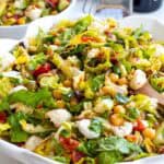 Fresh and colourful blood sugar-friendly salad with crunchy vegetables and cheese, perfect for a quick Mediterranean meal with a jar of dressing and more chopped salald in the background