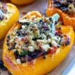Lentil stuffed pepper topped with golden halloumi, served in a white enamel baking tray with a blue rim. The vibrant roasted pepper is filled with a savoury lentil mix for an inviting, wholesome meal full of colour and texture.