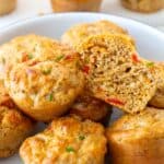 Gluten-free savoury muffins stacked in a white dish with a blue rime made with cheese, red pepper, and pesto, perfect for a blood sugar-friendly snack or lunchbox filler.