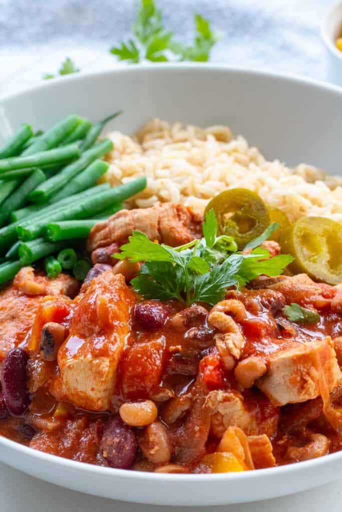 Family-friendly Mexican chicken bowl with jalapeños and brown rice, with corriander and blue cloth blurred in background