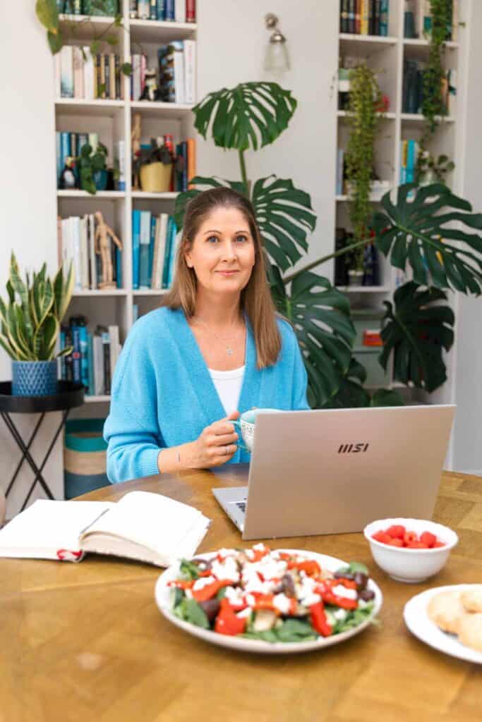 Michelle Rorke, founder of Whole Hearty Kitchen, smiling in front of her laptop with food and notebooks on the table - diabetes food blogger UK