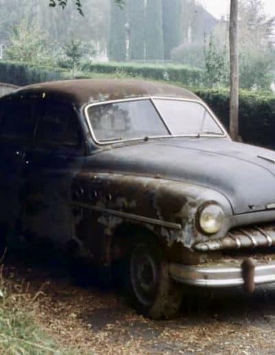 Rusty vintage car parked on the side of a road, showing signs of age and wear.