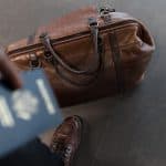 man holding a U.S. passport with a brown bag with his travel documents in it