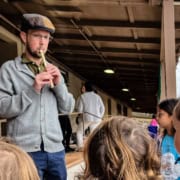 Quin Herron playing tin whistle with school children watching.