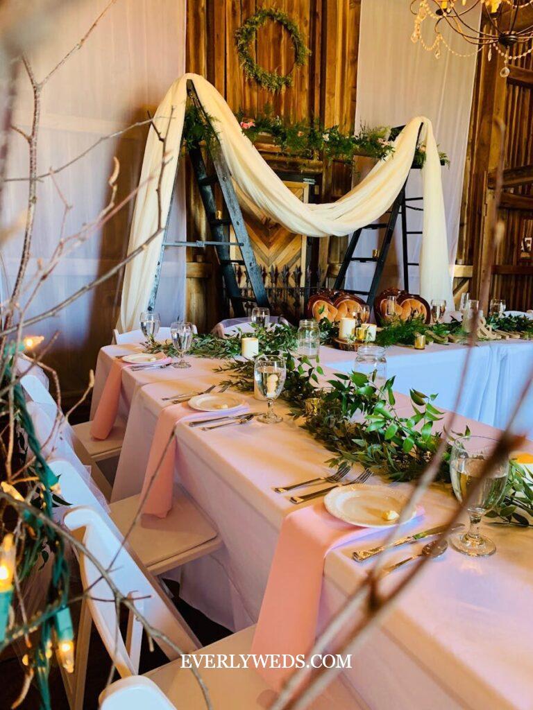Elegant rustic wedding reception with white draping, greenery garlands, and candles - budget-friendly backyard wedding decor ideas