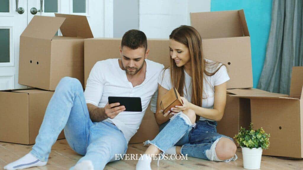 Young couple sitting among moving boxes looking at tablet and planning creative wedding gifts for their new home together