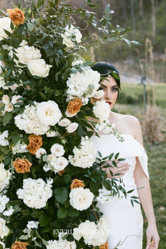 Bride with oversized white and orange floral arrangement - stunning budget wedding decoration idea for outdoor ceremonies