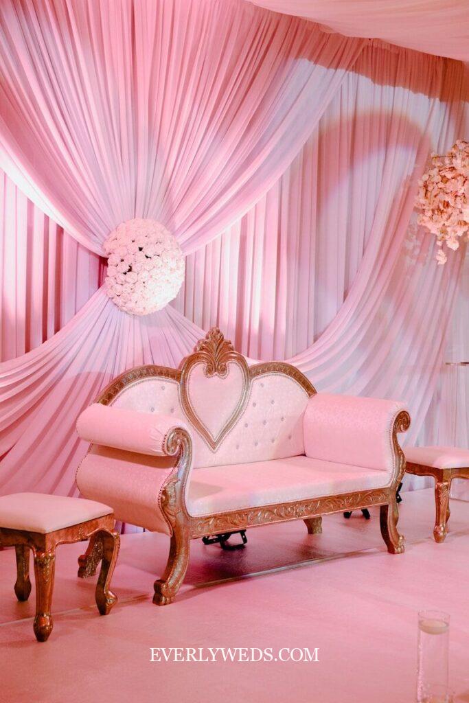 Pink draped fabric backdrop with ornate gold loveseat creates elegant budget wedding decor for small intimate ceremonies