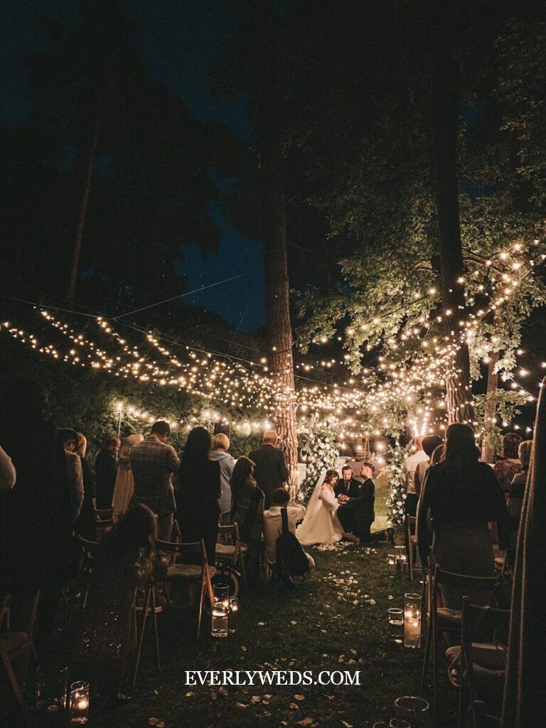 Stunning outdoor wedding ceremony with string lights and candles - affordable backyard wedding decoration ideas