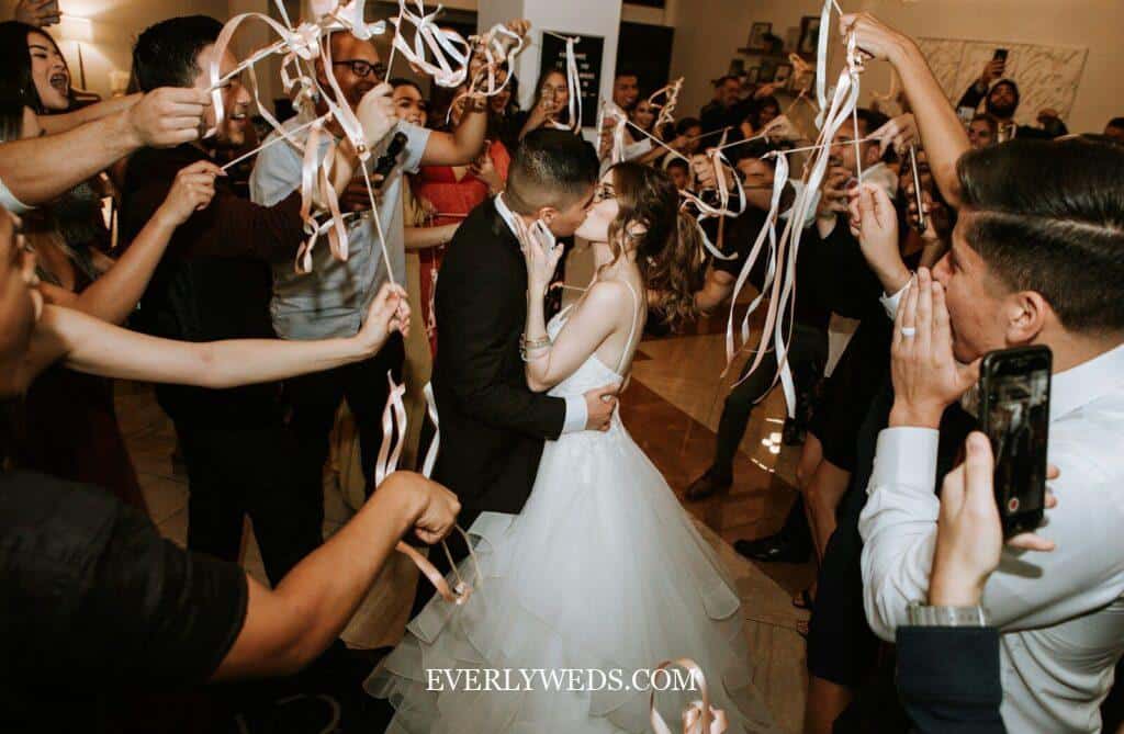 Bride and groom kissing surrounded by guests waving ribbon wands at wedding celebration
