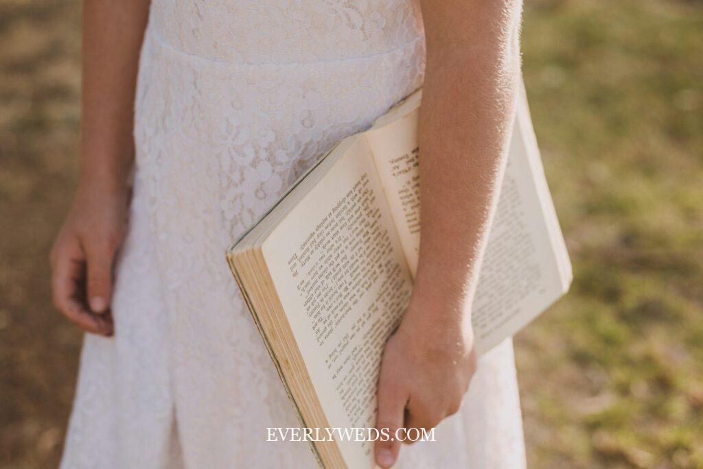 bridesmaid carrying vintage book wrapped in lace ribbon as non floral unique bridesmaid bouquet alternative for bookworm literary wedding