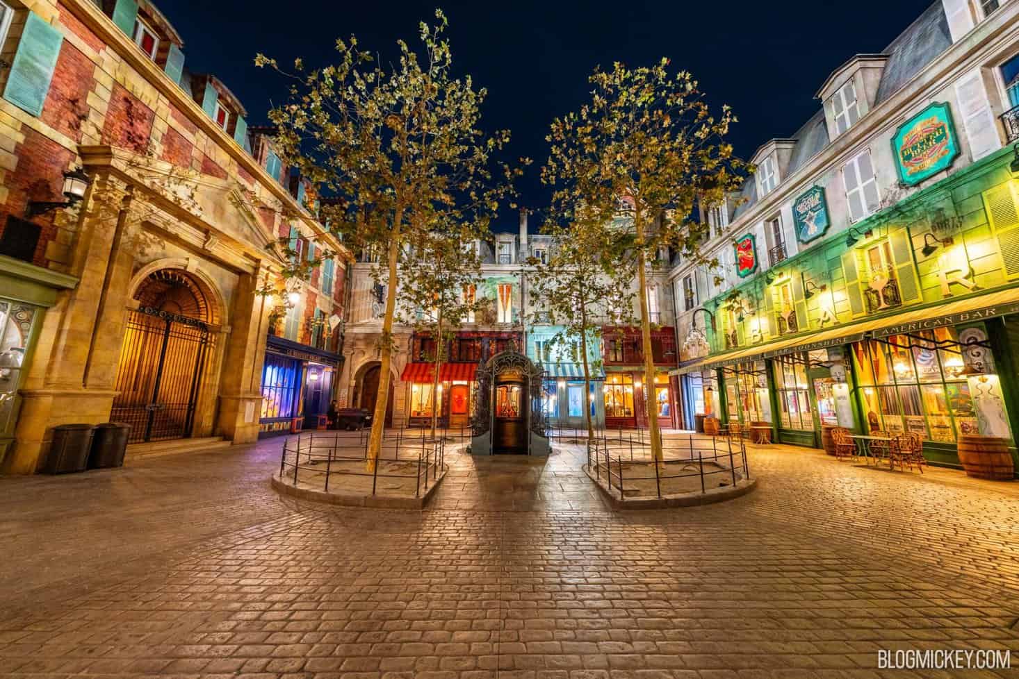 Colorful Epic Universe themed street at night with lit storefronts and trees.