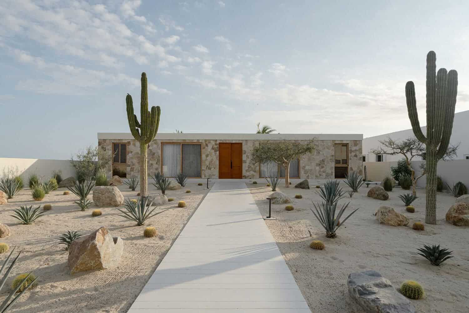 Desert landscape with modern minimalist house featuring desert plants and stone exterior, sunny sky, clean walkway, and natural materials for a stylish, sustainable architecture design.