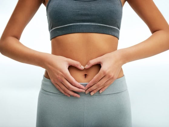 Fit woman in workout clothes making a heart shape with her hands over her abdomen