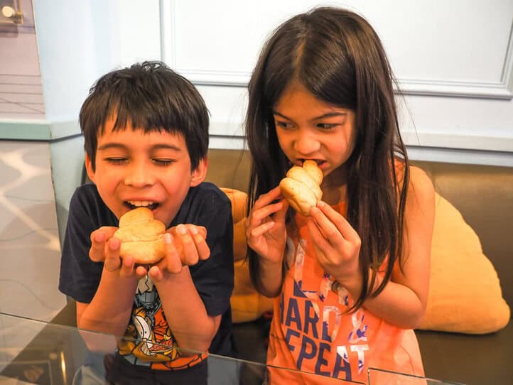 Dos niños mordiendo panecillos calientes en sus manos