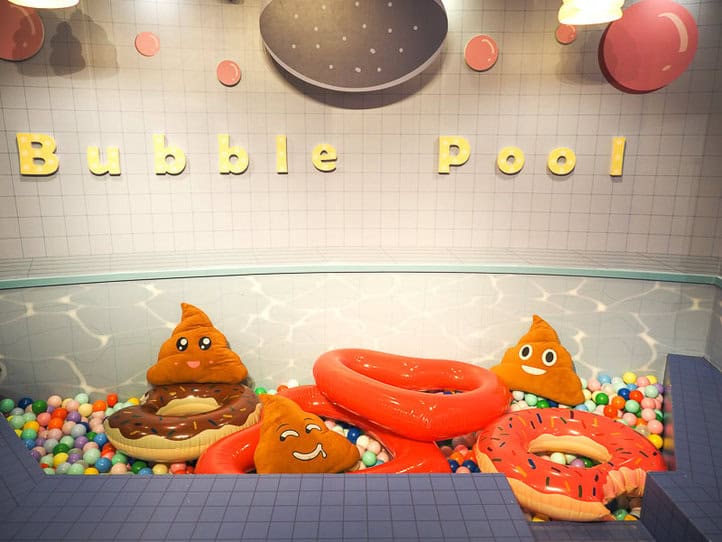 Una piscina de pelotas con varios peluches con forma de caca y las palabras "piscina de burbujas" en la pared de arriba.