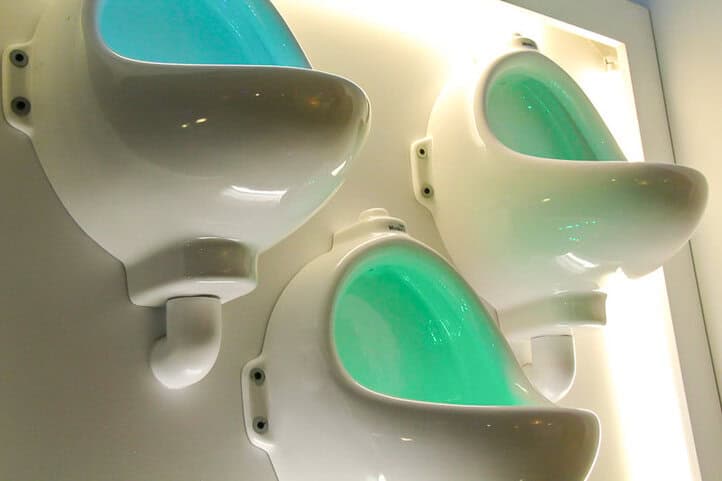 Tres inodoros de porcelana colgados en la pared de un baño como decoración, con luces verdes y azules que salen de su interior.